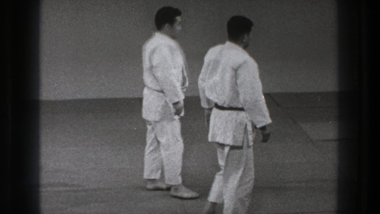 Two adult men in white judo gis stand on the tatami in a Tokyo training space, appearing to reset for another movement.
