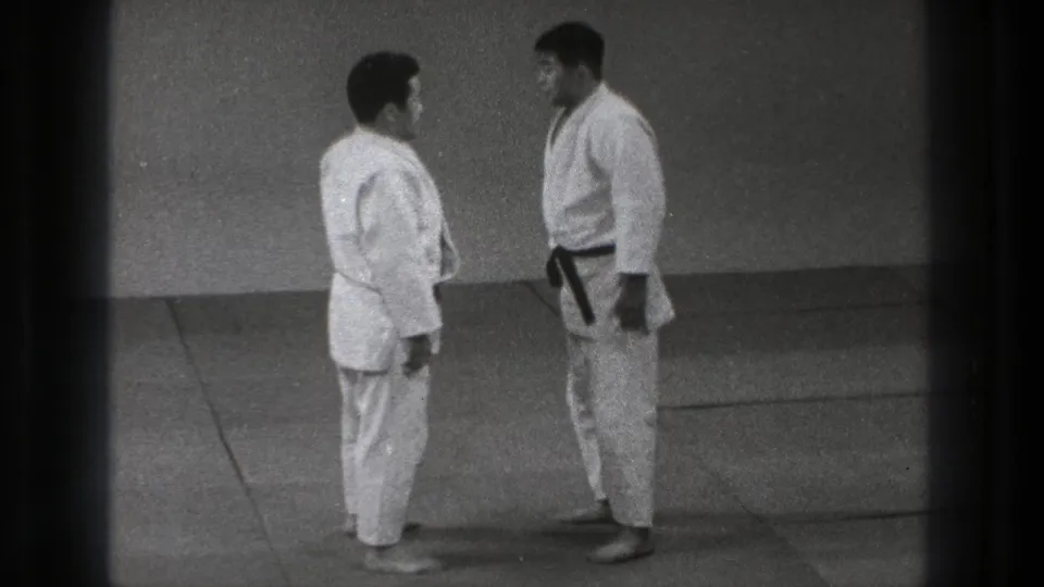 The 1971 Tokyo footage shows the practitioners squared up on the mat, with the dark-belted figure facing the other man.