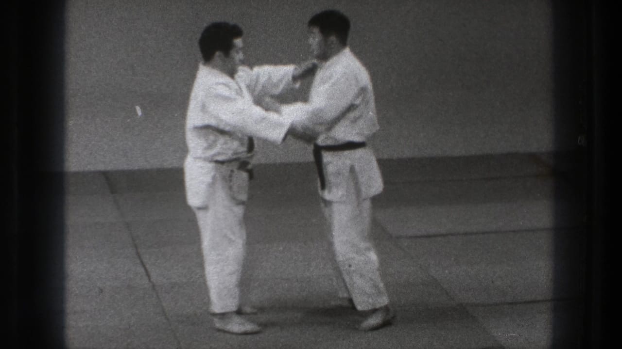 In the Tokyo dojo scene, the practitioners hold each other's gi as the demonstration moves into a controlled contact position.