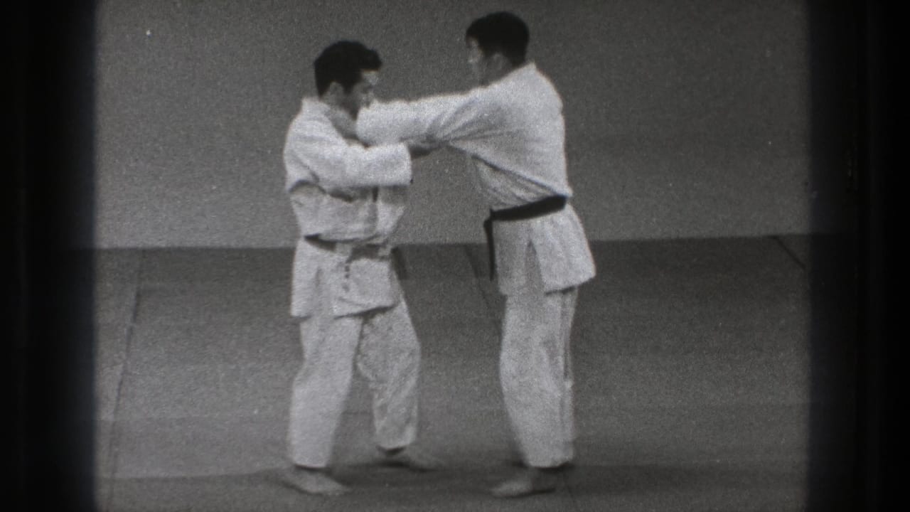In 1971 Tokyo footage, two barefoot martial artists in white uniforms face each other and grip sleeves on a dojo mat.