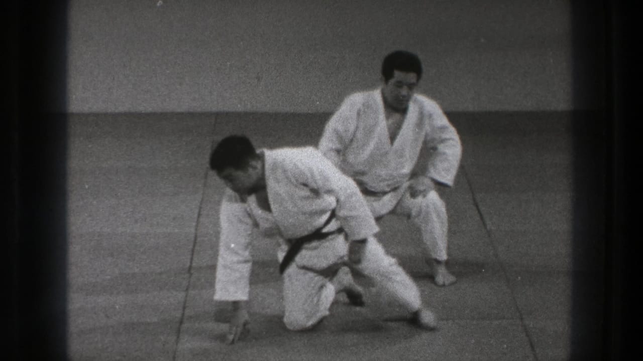 A martial arts practitioner rises to one knee as his partner remains seated on the tatami in 1971 Tokyo footage.