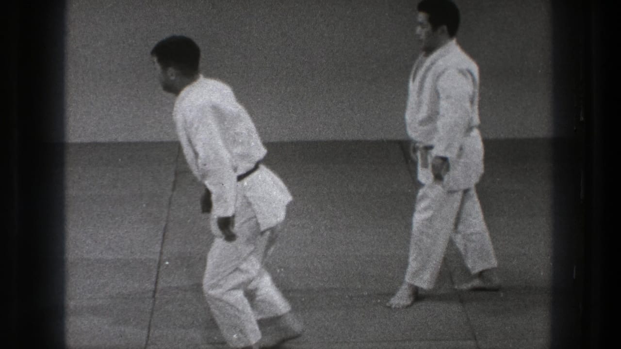 Two adult practitioners stand apart on the tatami, their white gi and belts visible in soft 8mm footage from Tokyo.