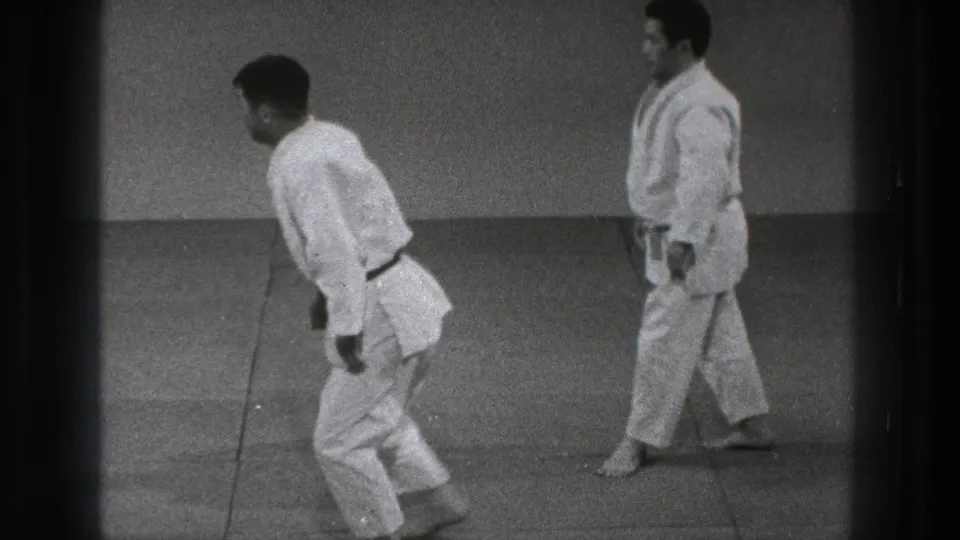 Two adult practitioners stand apart on the tatami, their white gi and belts visible in soft 8mm footage from Tokyo.