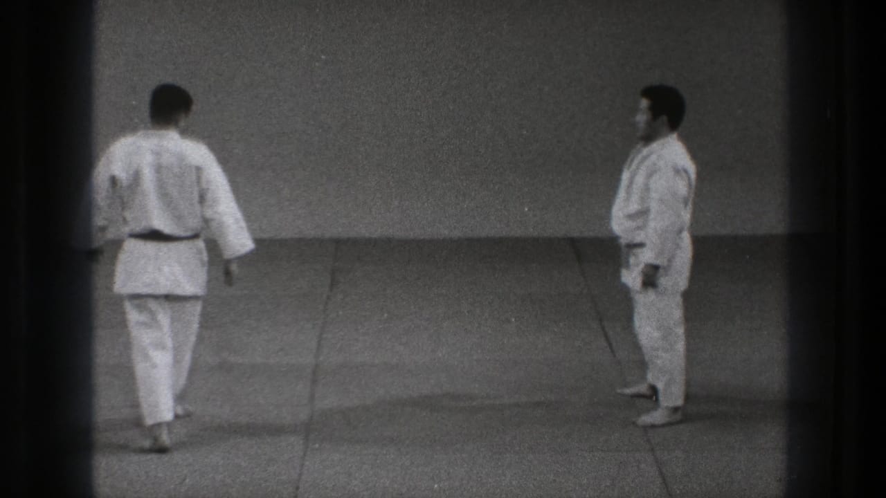 Two men in white martial arts uniforms stand on a grey mat.