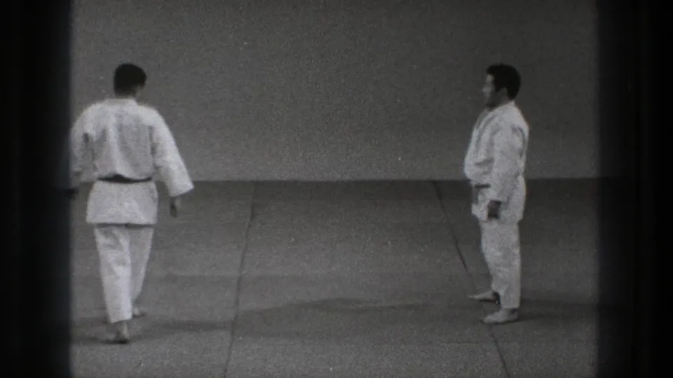 Two adult men in white martial arts uniforms stand apart on a grey mat in Tokyo, Japan, 1971 footage.