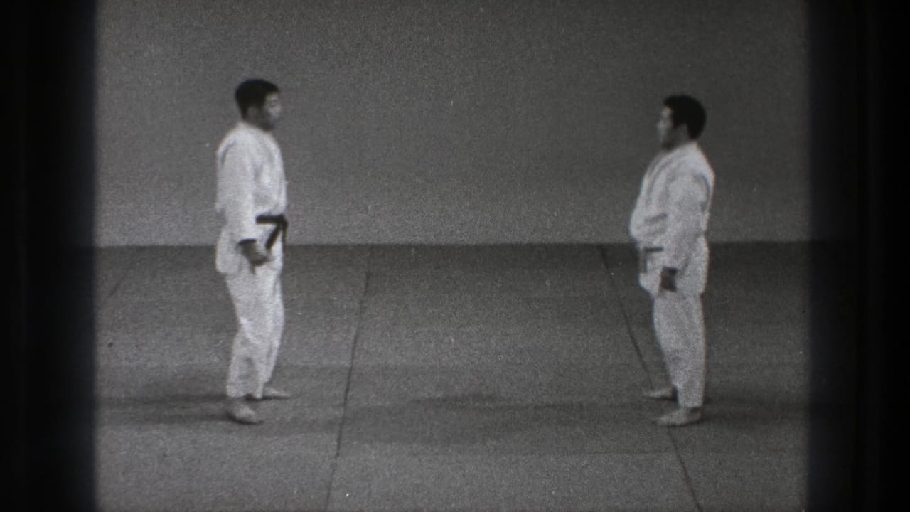 Two adult men in white uniforms face each other across a grey mat during a 1971 Tokyo martial arts demonstration.