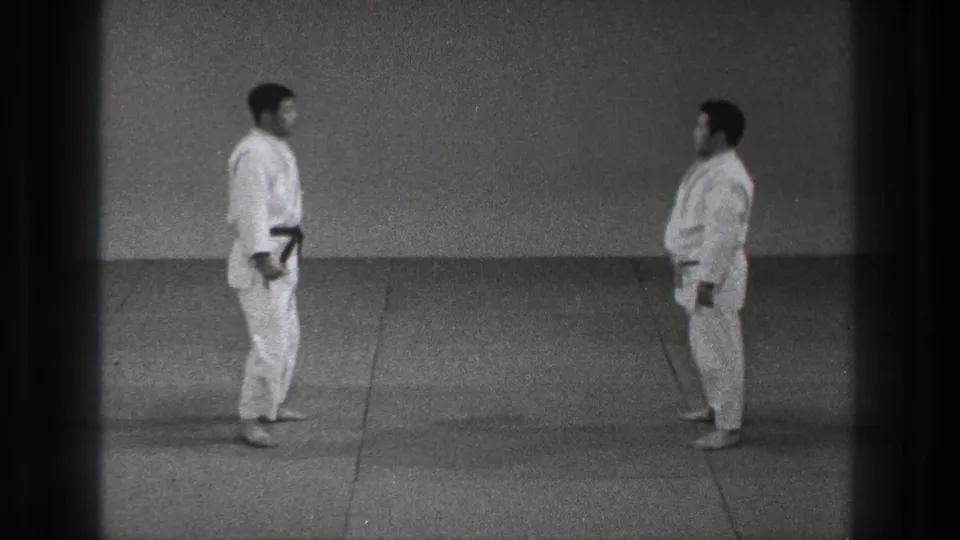 Two adult men in white uniforms face each other across a grey mat during a 1971 Tokyo martial arts demonstration.