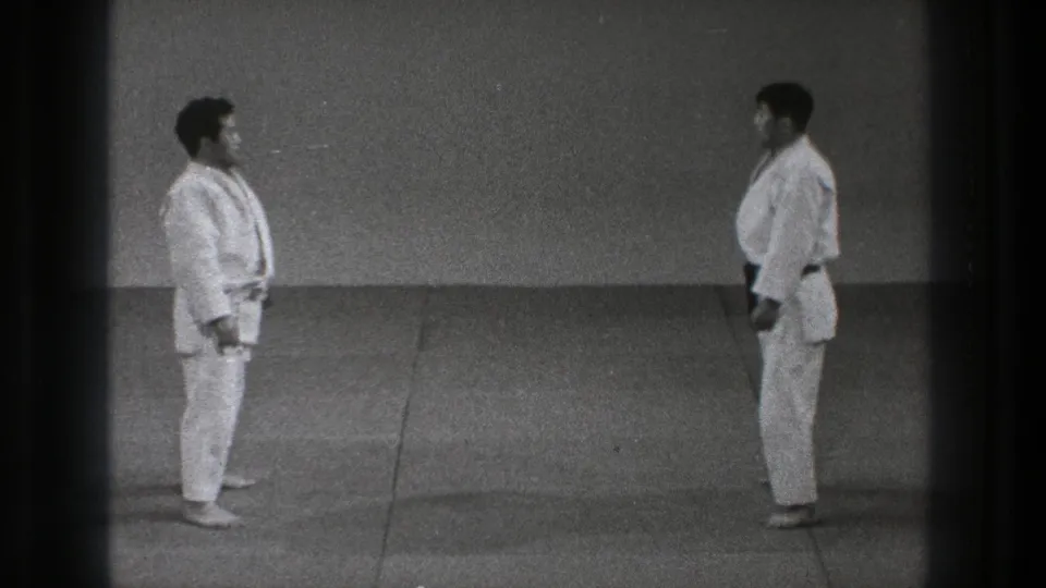 The 1971 Tokyo home-movie frame shows two men in gi standing opposite each other on a simple dojo mat before practice resumes.