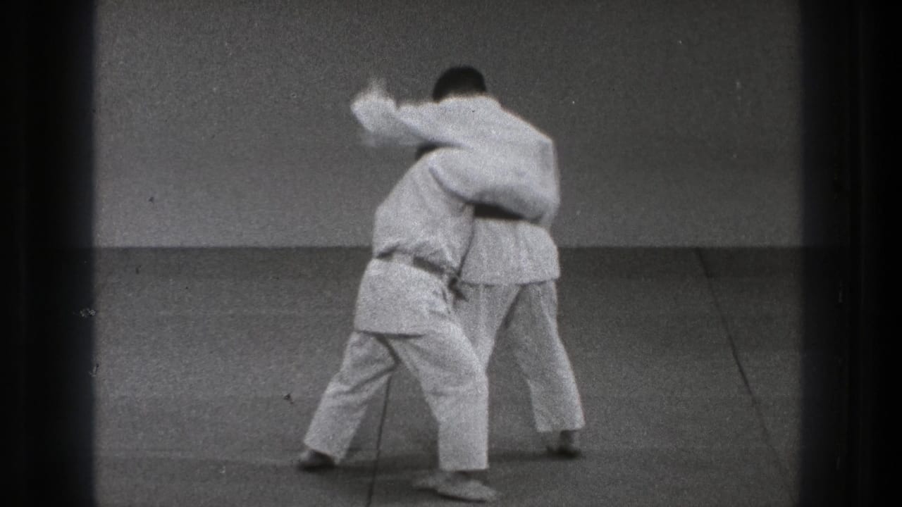 Two adult practitioners in white gi move into close body contact on the mat during a karate training sequence in Tokyo, 1971.