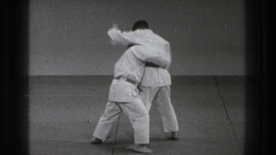 Two adult practitioners in white gi move into close body contact on the mat during a karate training sequence in Tokyo, 1971.