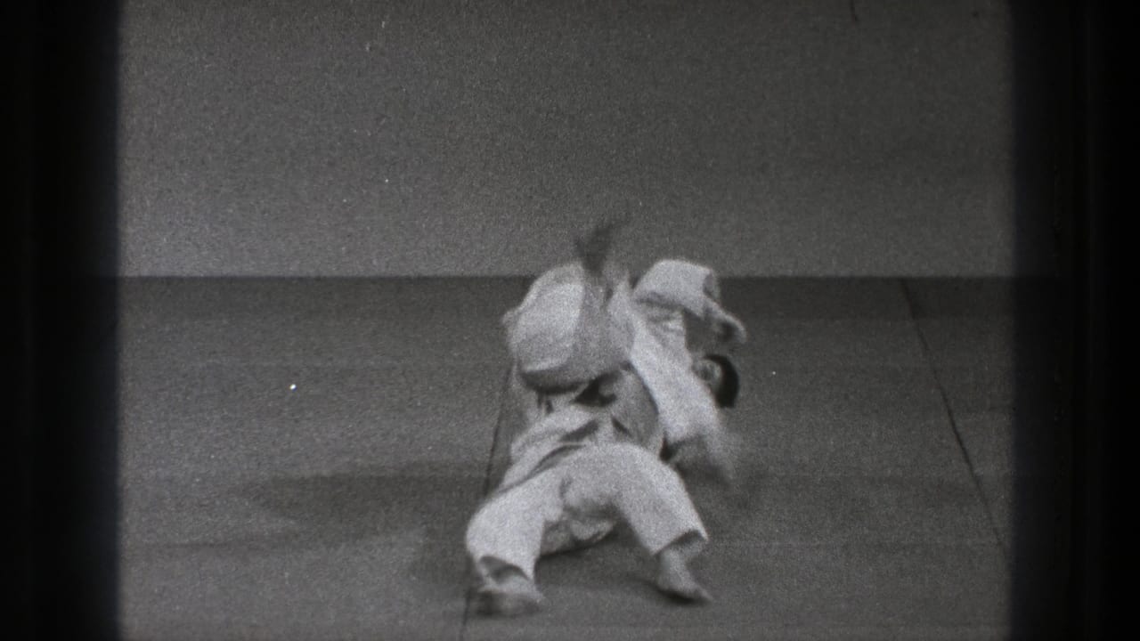 During the 1971 Tokyo practice, one man in a white gi is taken down on the mat while the other remains over him in motion.