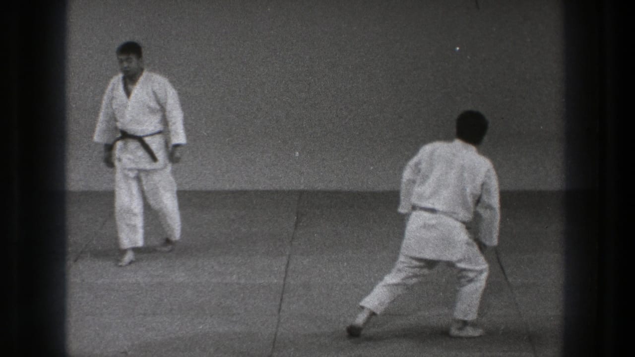 1971 Tokyo karate practice frame showing two adults in white gi facing each other, with one moving forward in a low stance.