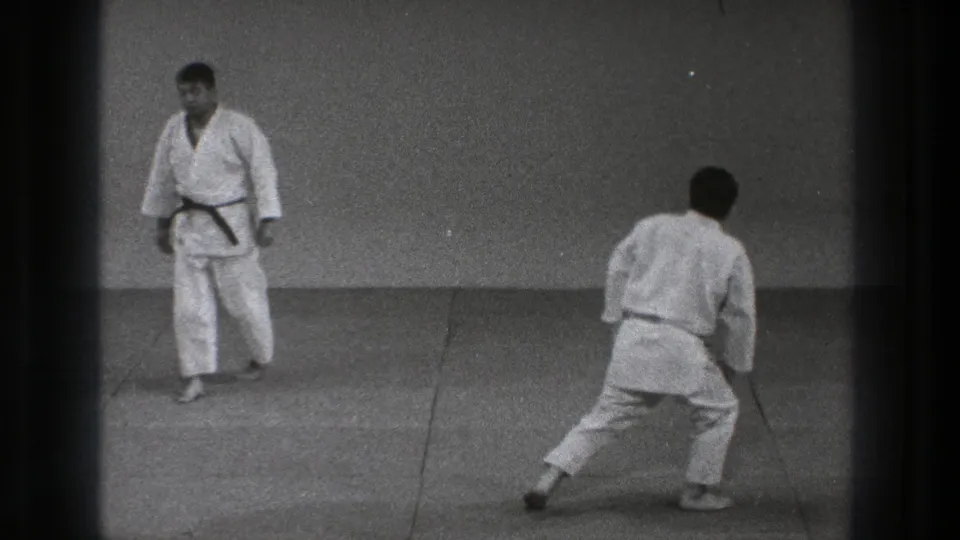 1971 Tokyo karate practice frame showing two adults in white gi facing each other, with one moving forward in a low stance.