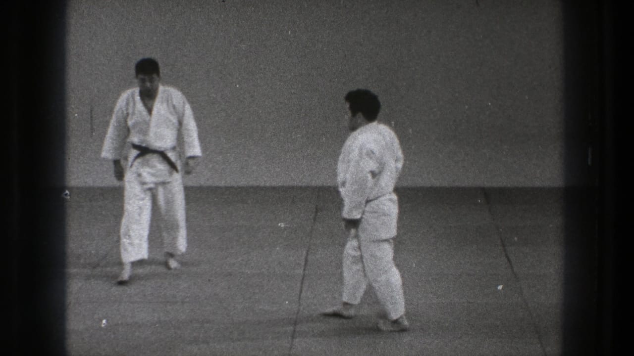1971 Tokyo karate practice frame with two adult practitioners in white gi standing face to face on a simple indoor mat.
