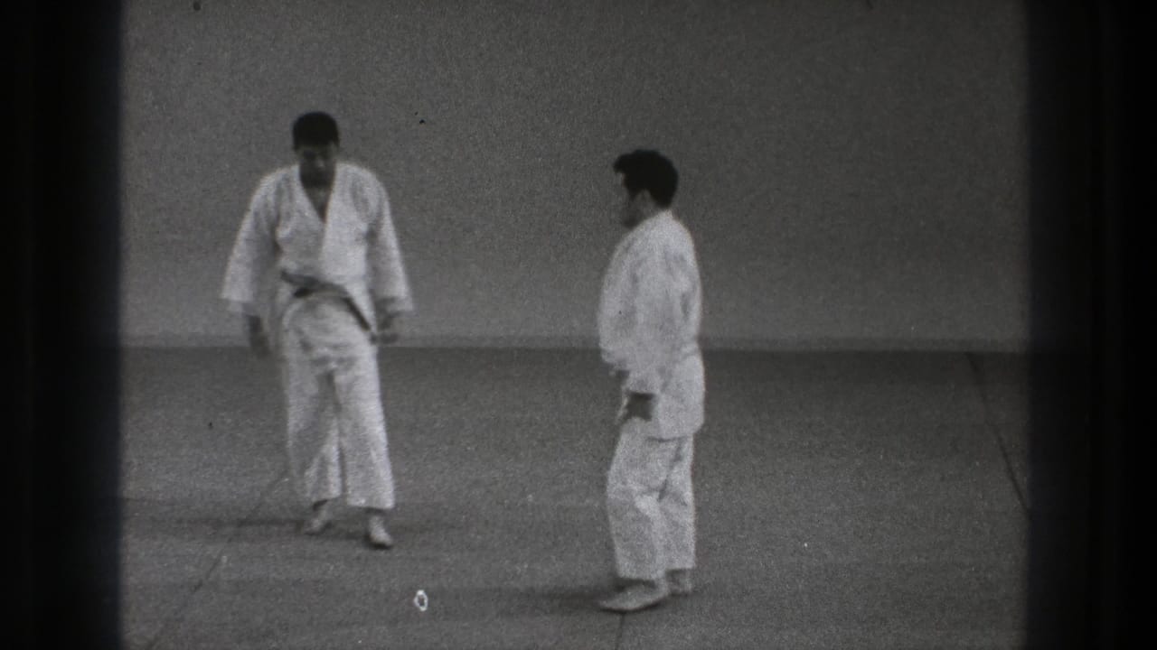 Two karate practitioners in white gi face each other on a mat.
