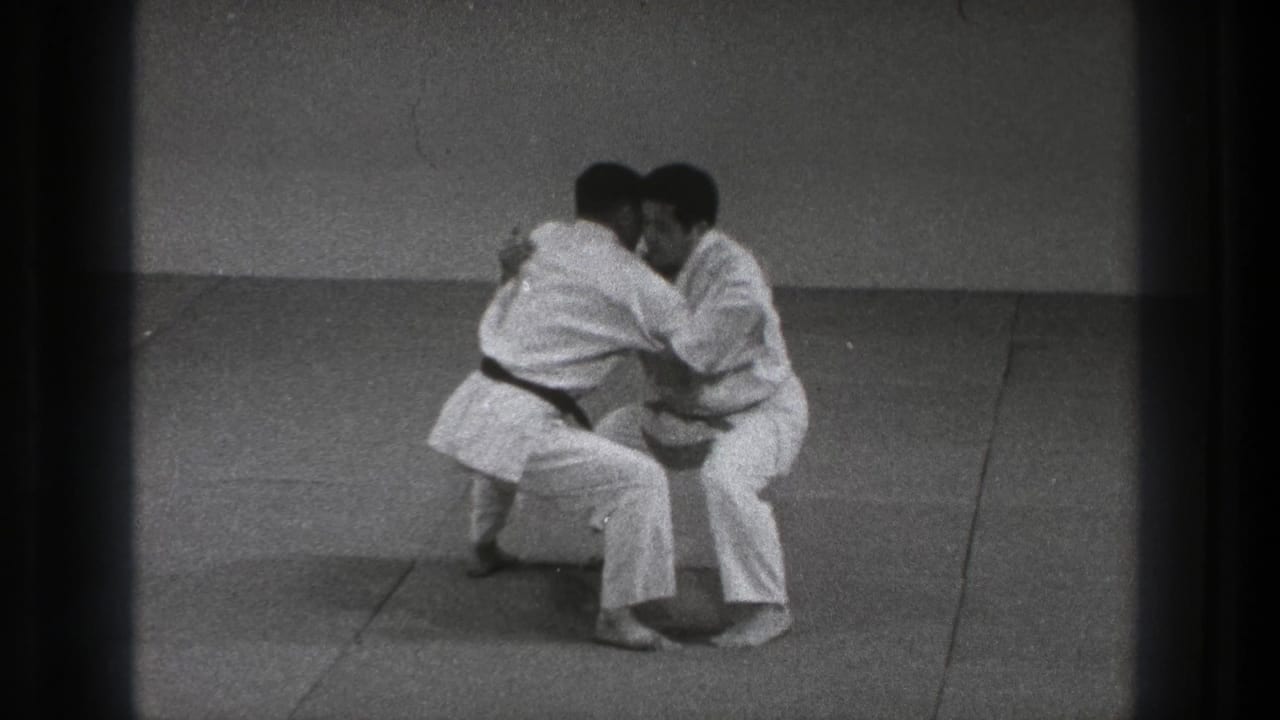 Two adult karate practitioners in Tokyo, 1971, maintain a tight grappling hold while lowering their stance.