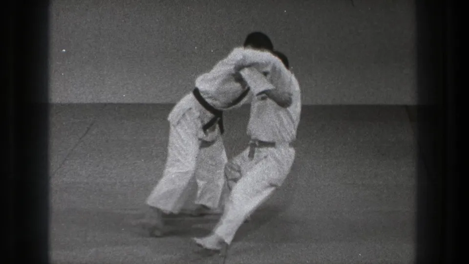 Near the end of the 1971 Tokyo clip, one karate practitioner draws the other into an off-balance takedown motion.