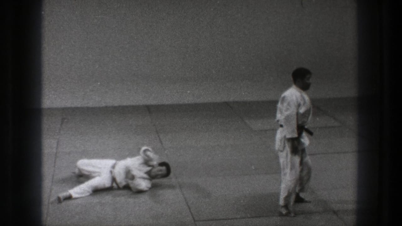 One martial artist lies on the mat while another stands nearby.