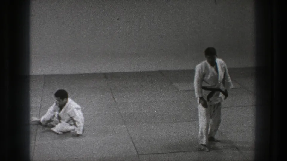 Tokyo 1971 8mm frame showing one martial artist seated on the mat and another standing after practice movement.