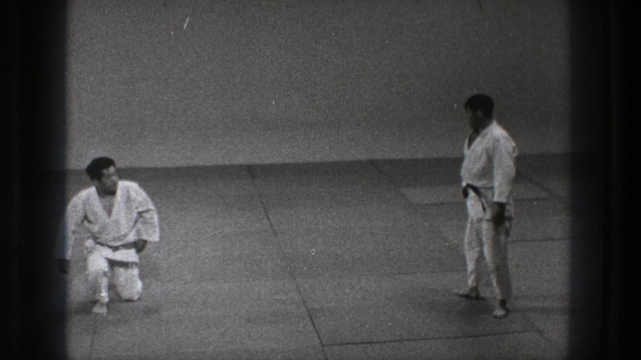 Tokyo 1971 8mm frame with one martial artist kneeling and another standing across the dojo mat.