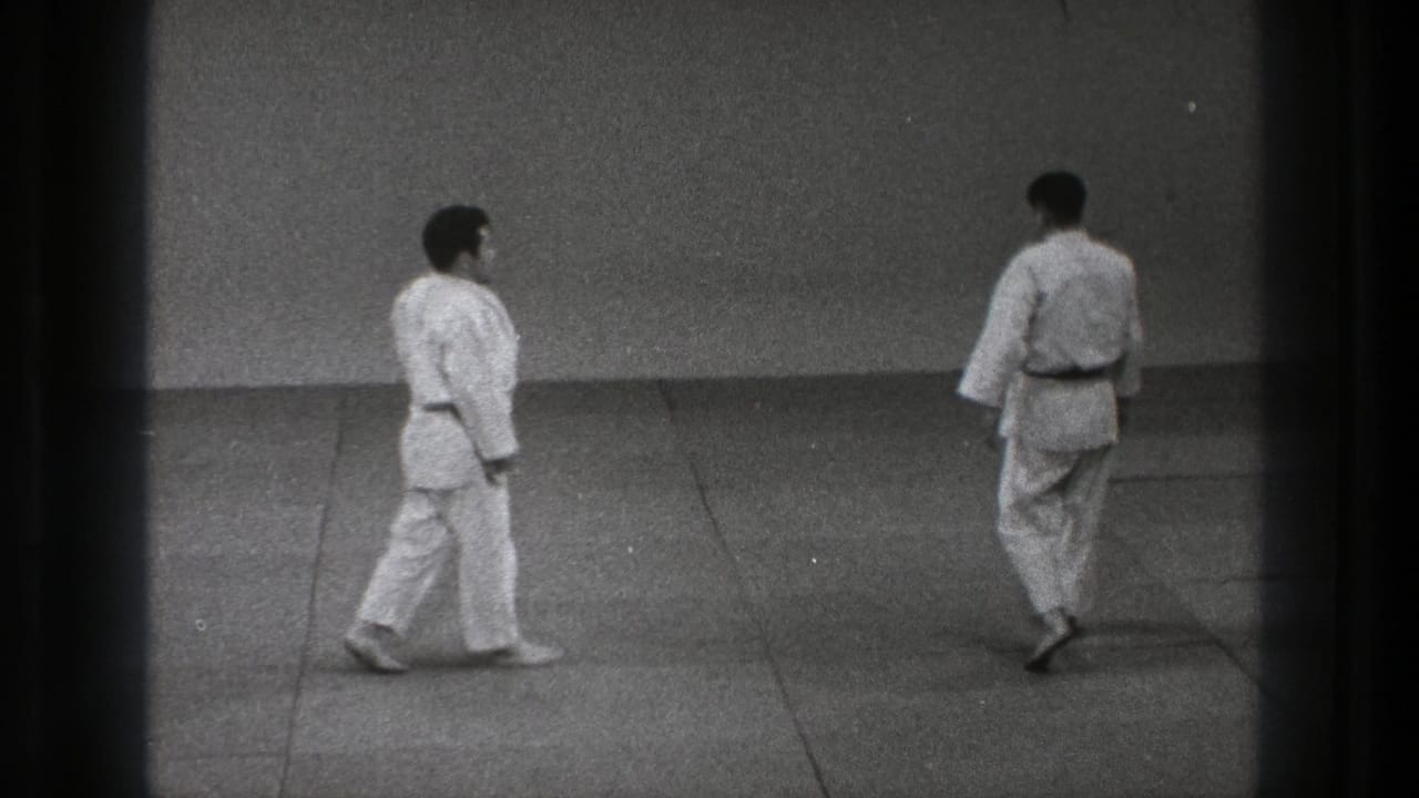 Adult martial artists in white gi move across a dojo mat in grainy 8mm footage from Tokyo, 1971.