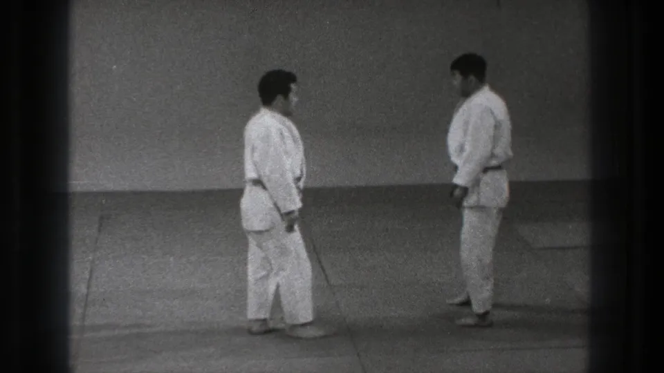 Two adult martial artists in gi stand face to face on a dojo mat during a formal pre-match moment in Tokyo, 1971.