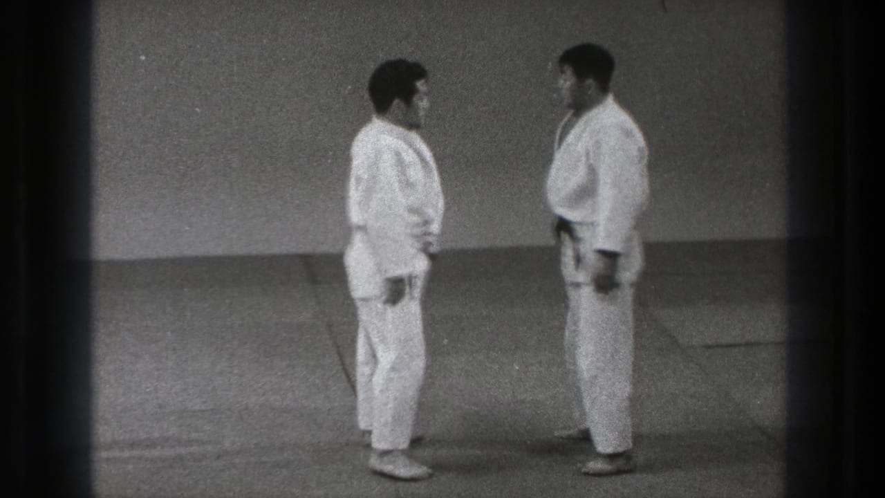 Grainy 8mm frame of two adult martial artists in white gi holding a close face-to-face stance in Tokyo, 1971.