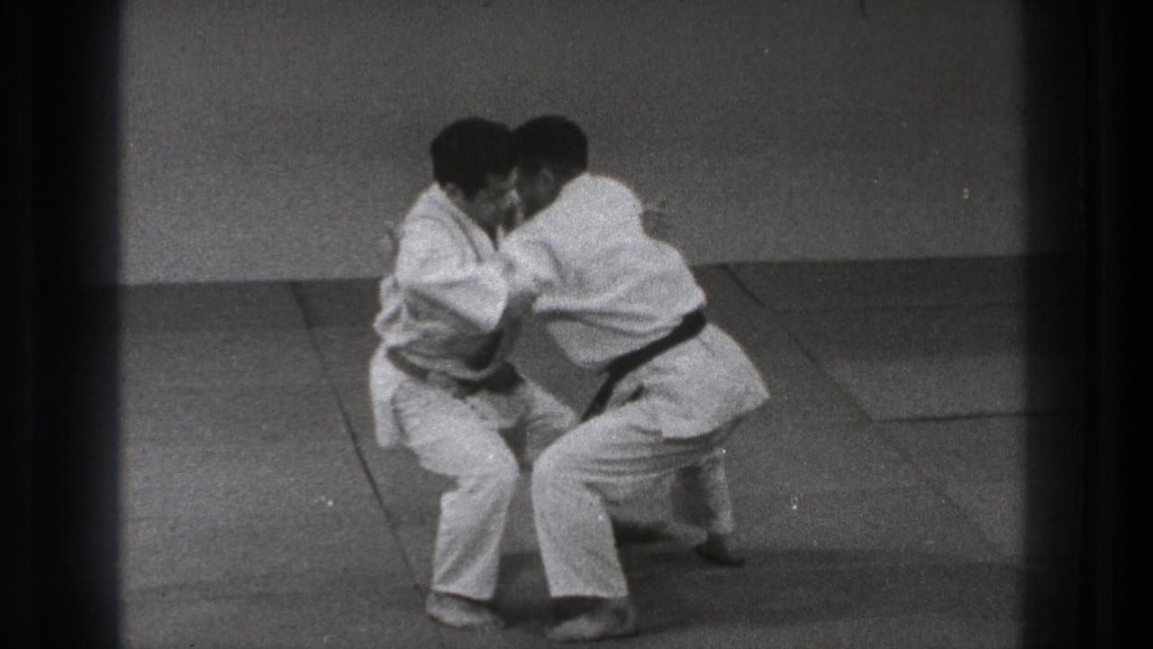 The practitioners lower their stance during the Tokyo 1971 demonstration, with arms engaged around the torso and sleeves as the move develops.