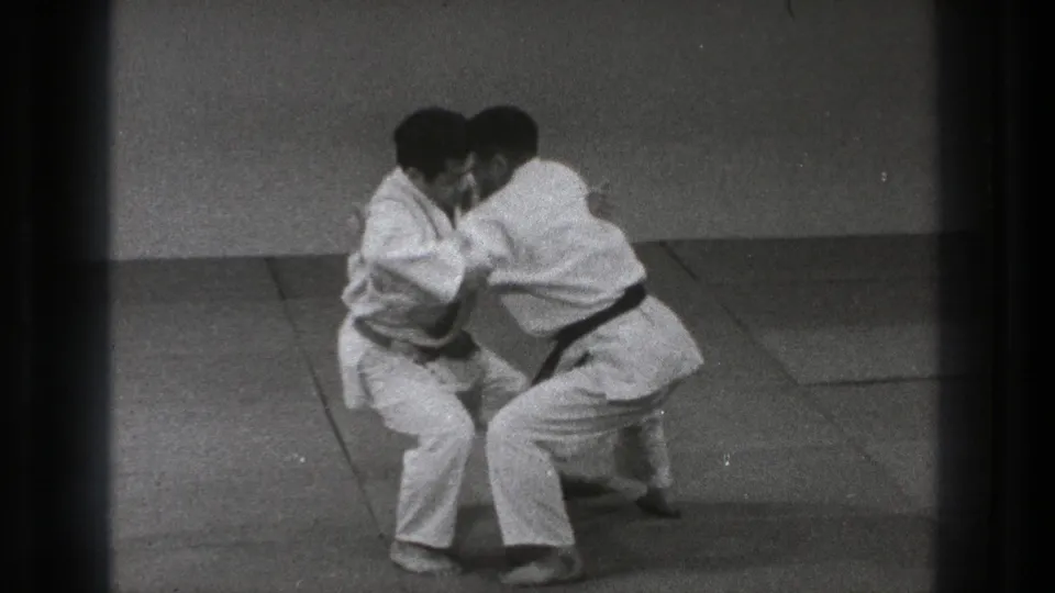 The practitioners lower their stance during the Tokyo 1971 demonstration, with arms engaged around the torso and sleeves as the move develops.
