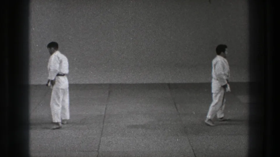 1971 Tokyo dojo footage showing two adult karate practitioners in white gi near the end of a brief training movement.