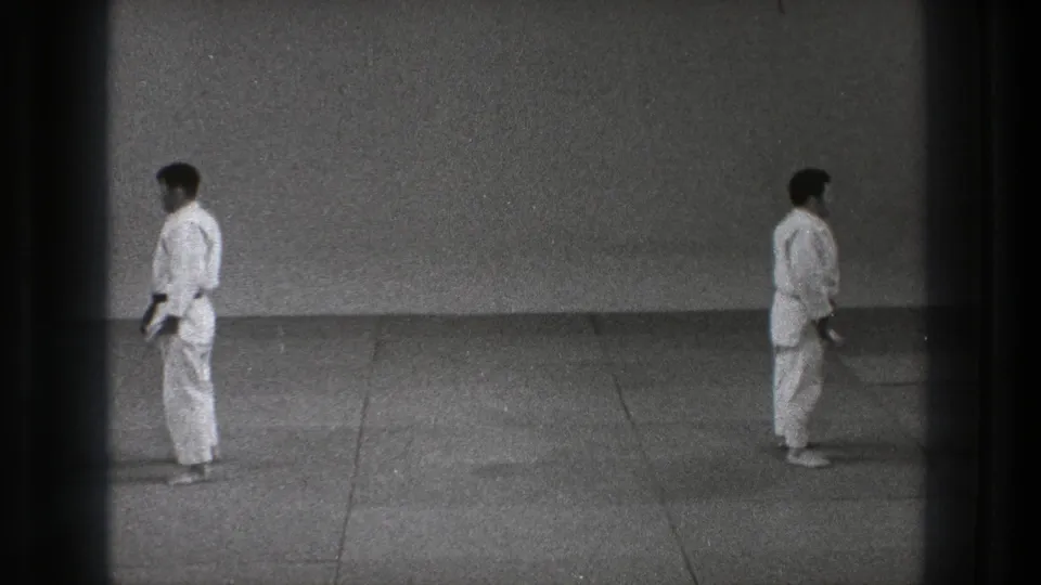 In Tokyo 1971 footage, two karate practitioners in white gi stand in formal stances across a plain dojo-like space.