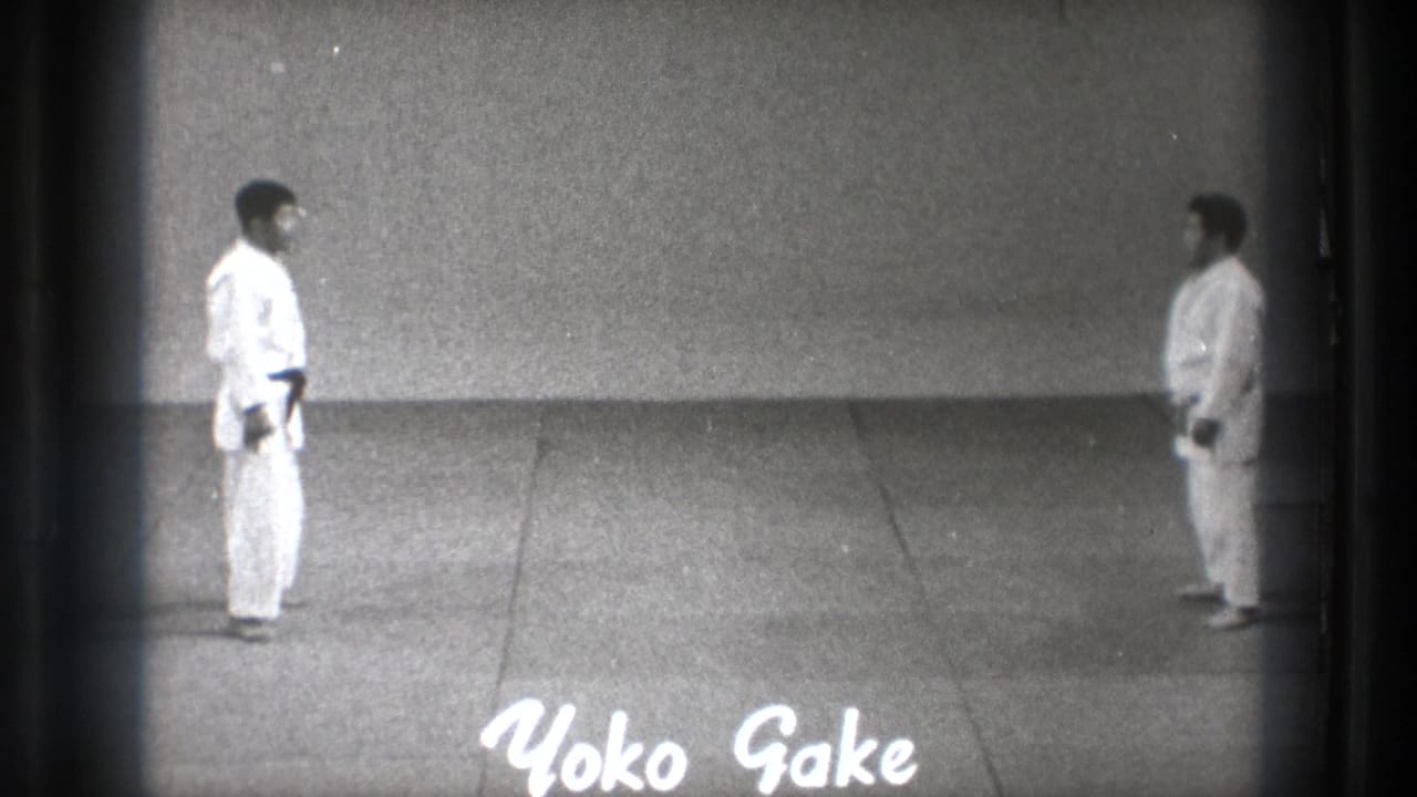 Two martial artists in white gi stand apart on a mat with Yoko Gake text at the bottom.