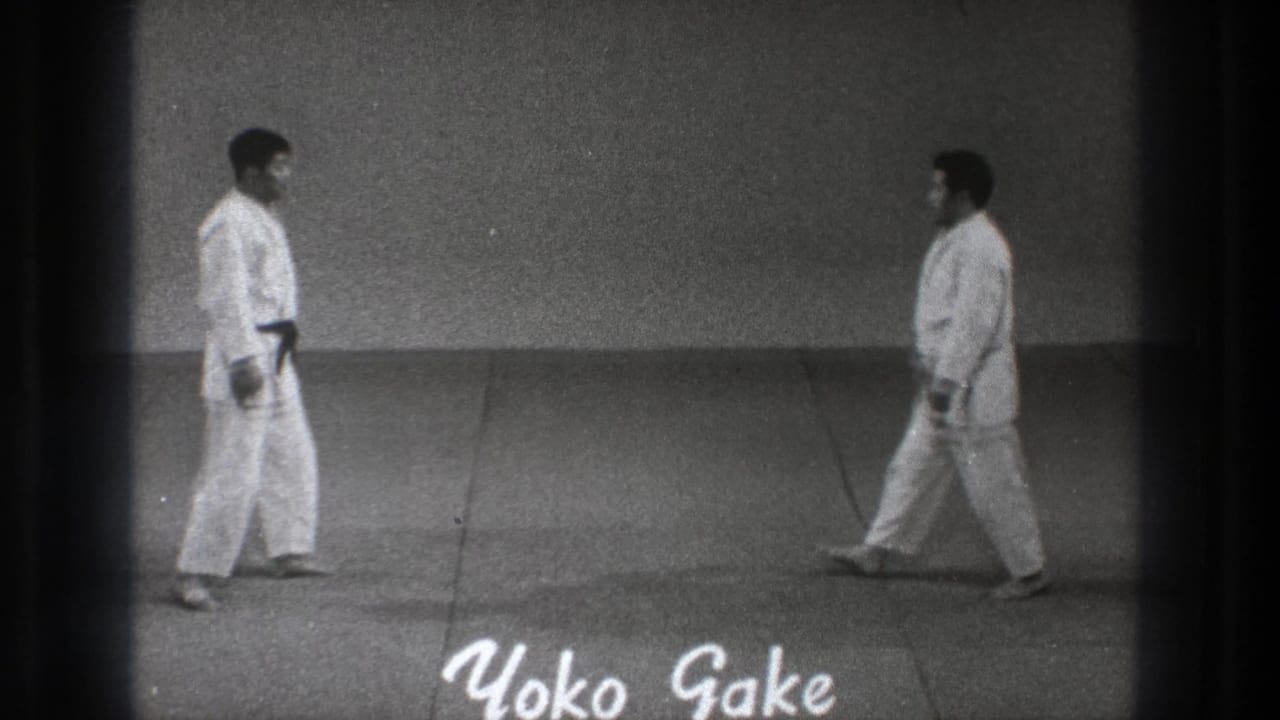 Two martial artists in white gi walk toward each other on a plain mat.