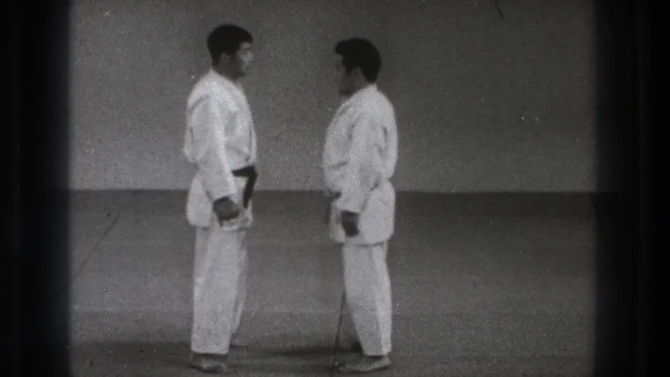 The 1971 Tokyo martial arts footage shows two adult practitioners face to face on a simple mat, framed by dark 8mm film edges.