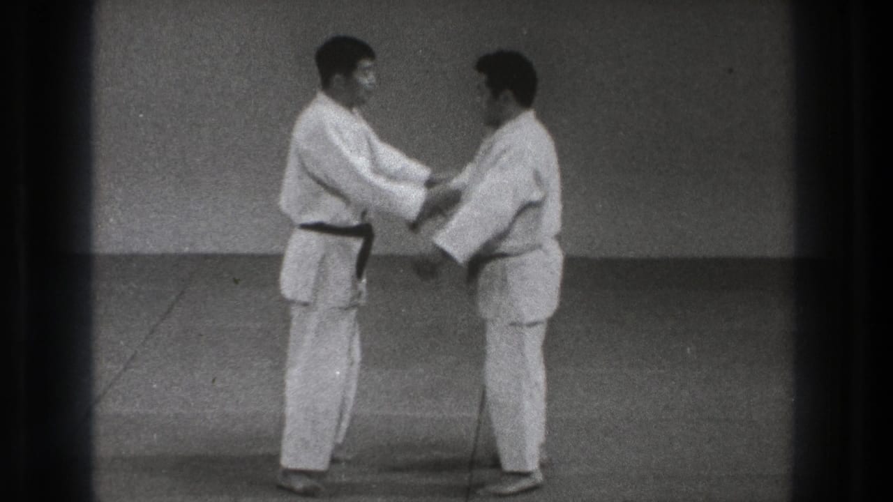 Two men in white martial arts uniforms face each other on a mat and hold each other's sleeves.