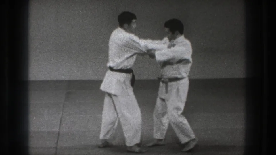 The 1971 Tokyo footage shows two adult martial arts practitioners stepping through a close-range technique, with their feet and body weight shifting on the mat.