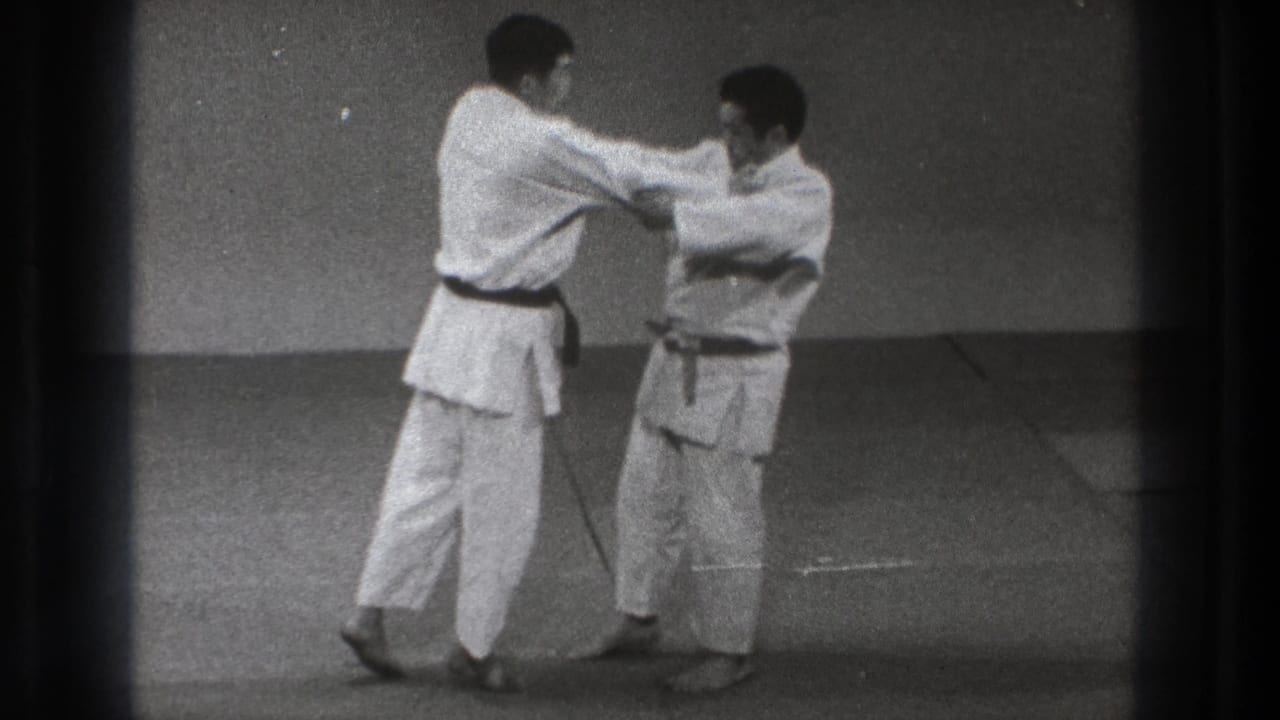 Two men in white gi grip each other while standing on a mat.