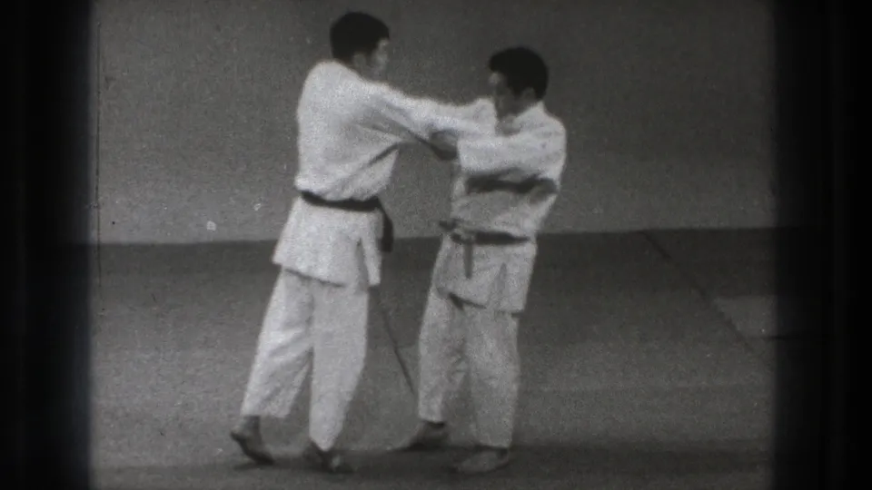 The two practitioners remain upright in a controlled grip position during the Tokyo martial arts practice sequence.