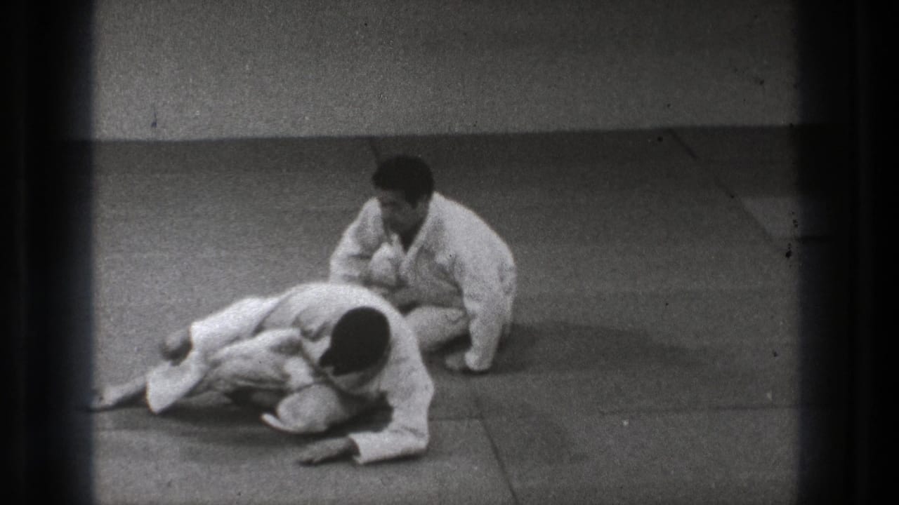 A kneeling practitioner in a white gi controls a second man lying forward on the mat during the 1971 Tokyo martial arts demonstration.