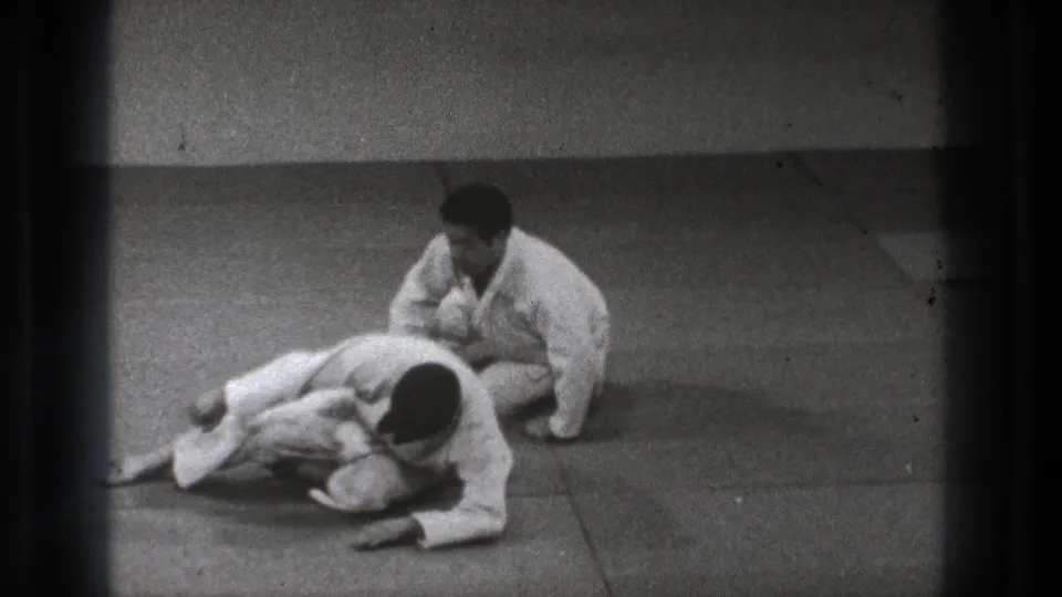 A kneeling practitioner in a white gi controls a second man lying forward on the mat during the 1971 Tokyo martial arts demonstration.