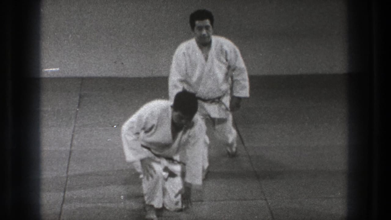 At the end of the short sequence, two adult practitioners in white gi begin to rise from the mat in the Tokyo training space.