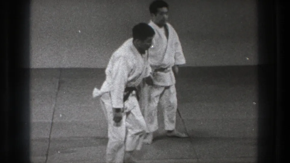 Two adult martial artists in white gi and black belts practice on mats in Tokyo, Japan, in 1971 home-movie footage.