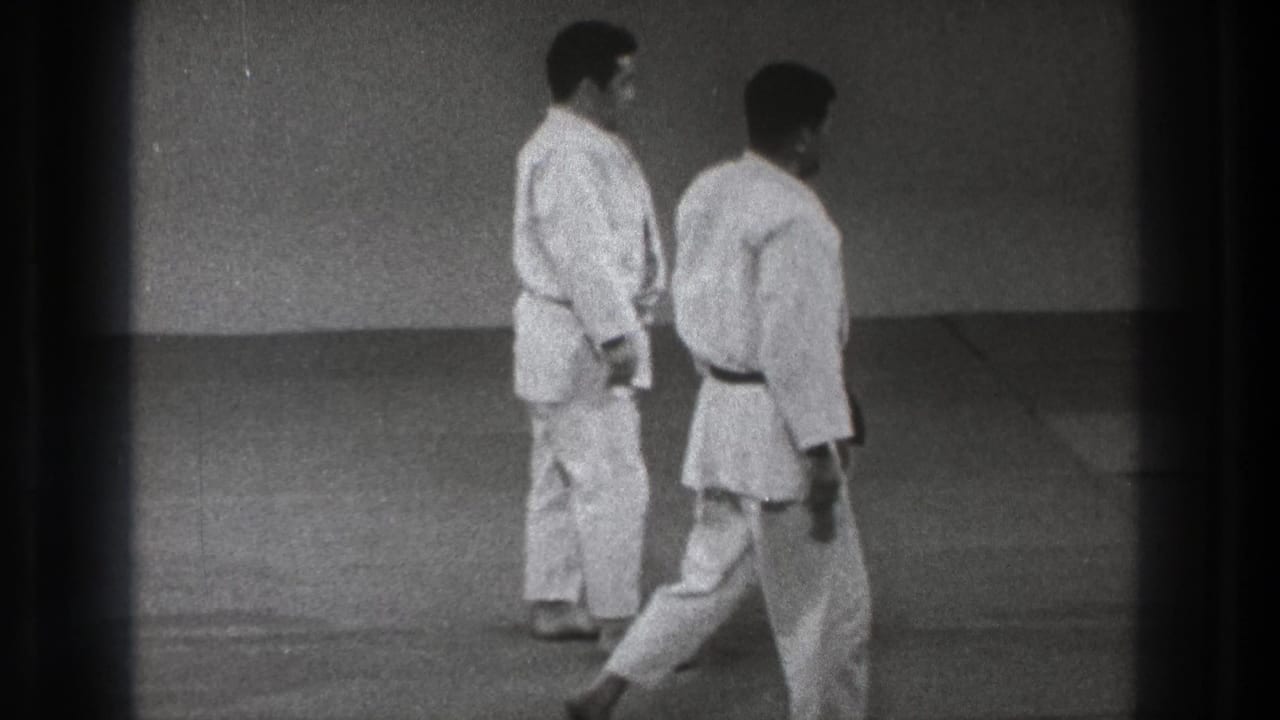 Two adult judo practitioners in white gi move across an indoor mat in 1971 Tokyo home-movie footage.