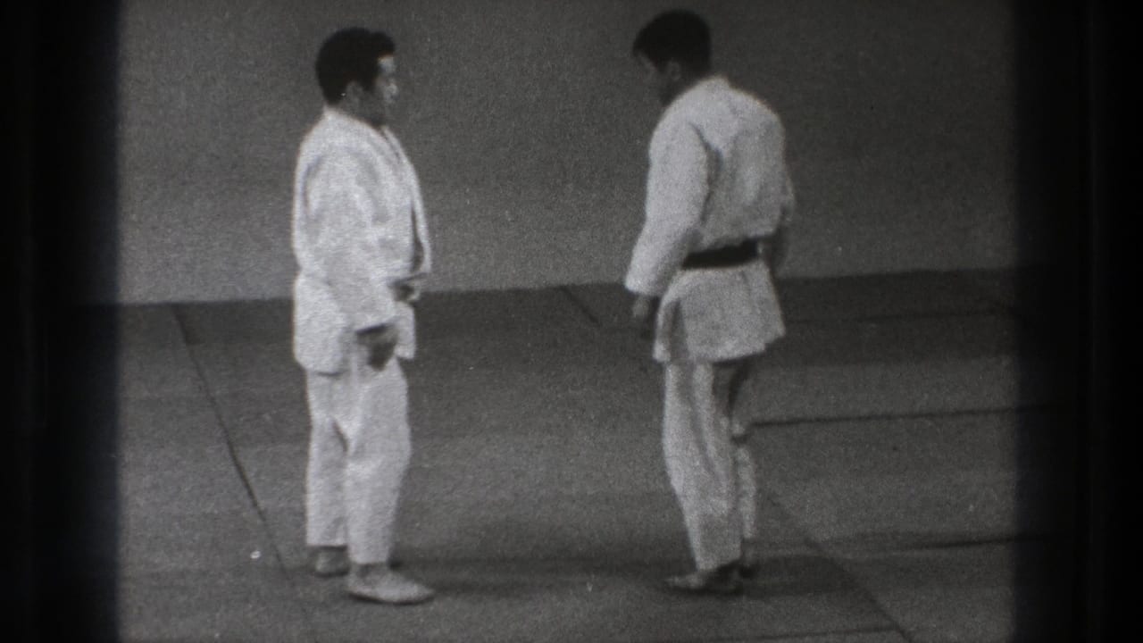Two adult judo practitioners face each other on an indoor mat in grainy 1971 Tokyo 8mm footage.