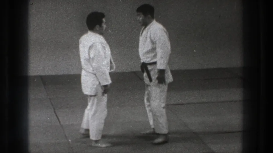 Two adult men in white karate gi face each other on mats in 1971 Tokyo martial arts practice footage.
