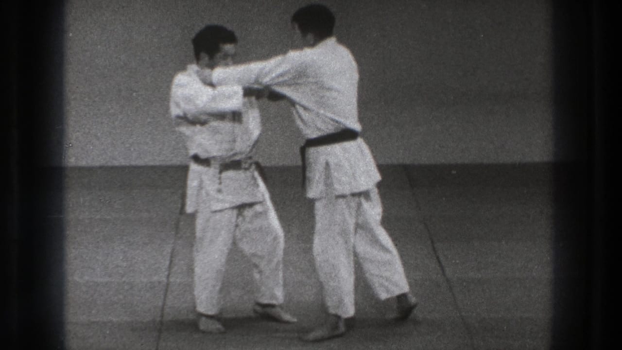 Two martial artists in white gi grip each other on a mat.
