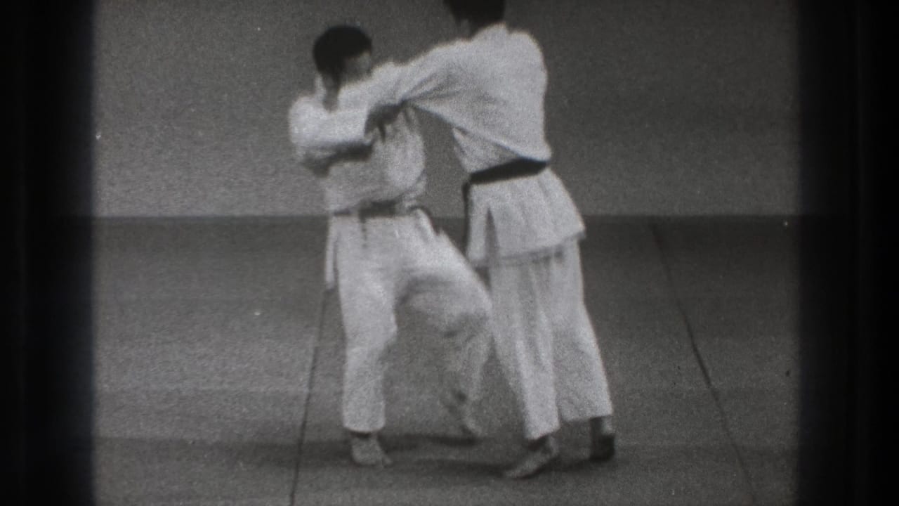 In the 1971 Tokyo judo sequence, one practitioner raises a leg while maintaining grips during the setup for a throw.