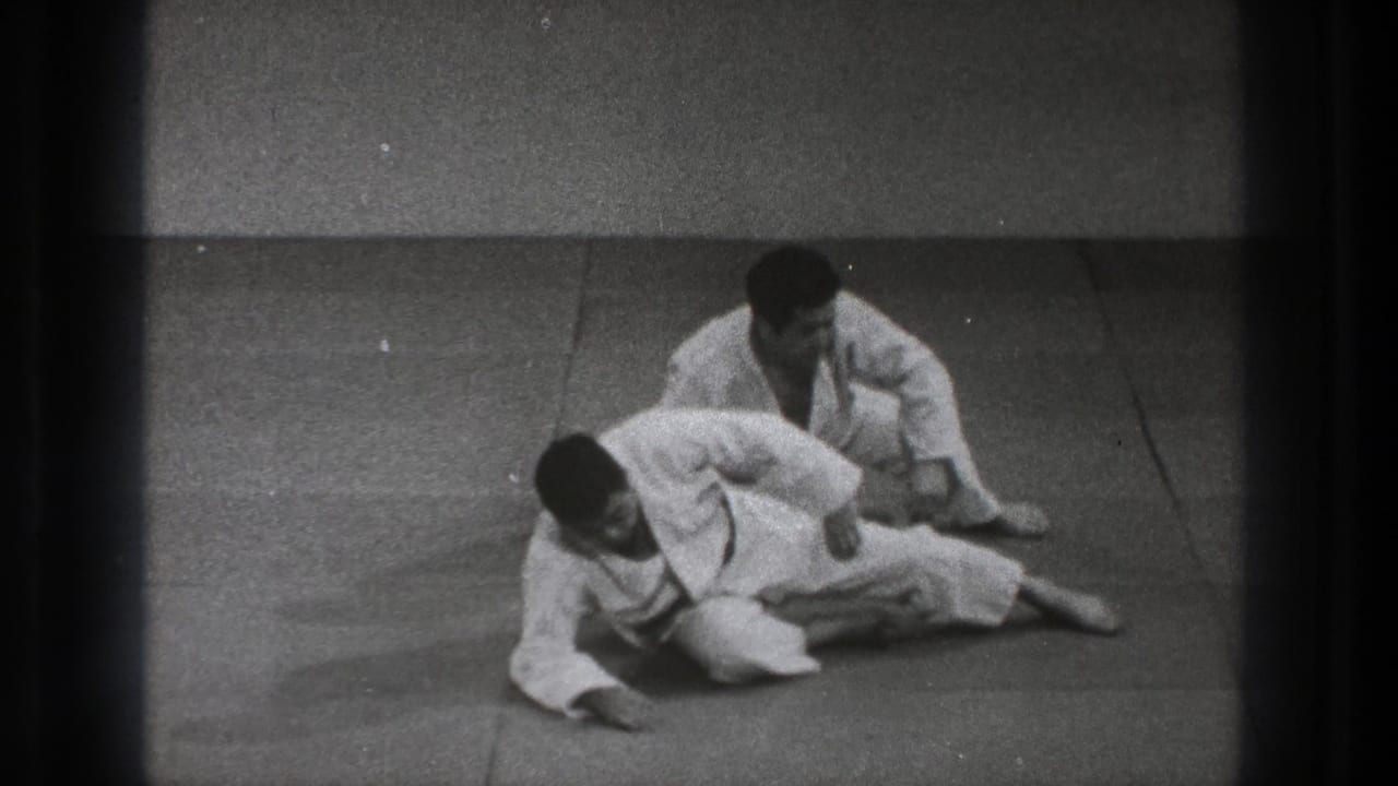 The practitioners transition from a low hold, with one seated behind the other on the mat in the 1971 Tokyo training footage.