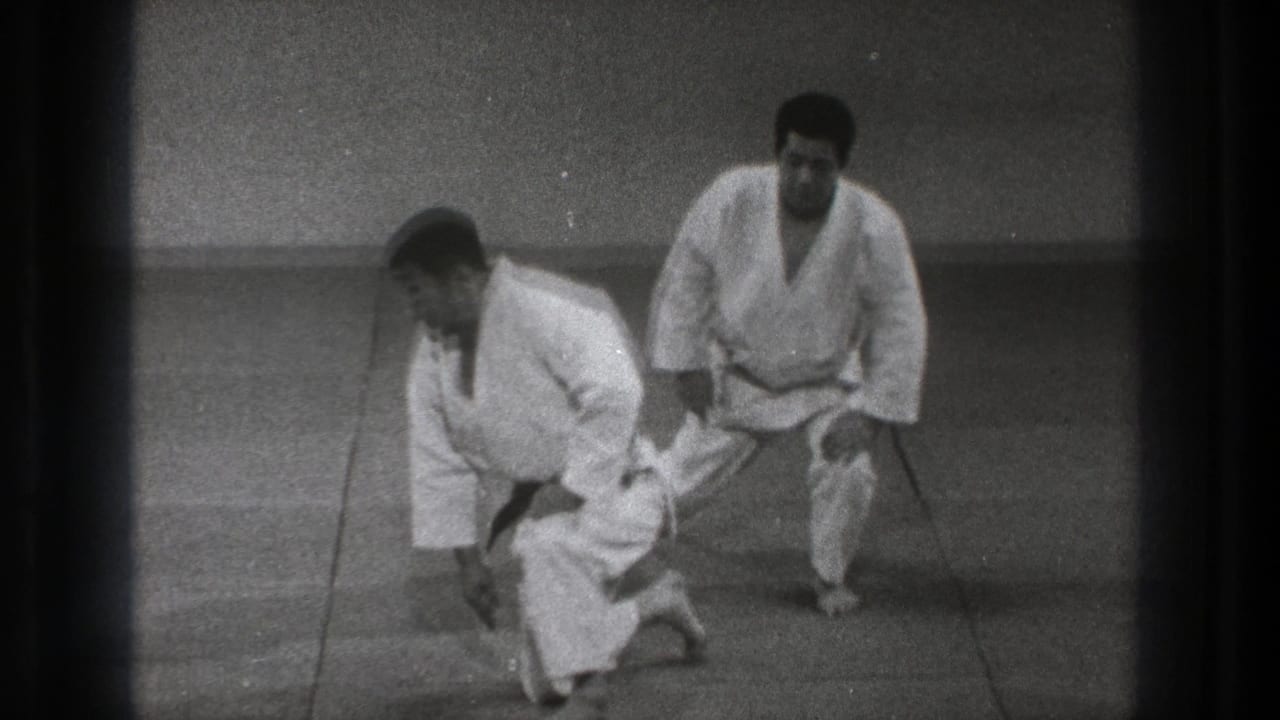 Near the end of the clip, two adult martial artists in white uniforms begin to stand after completing the grounded drill.