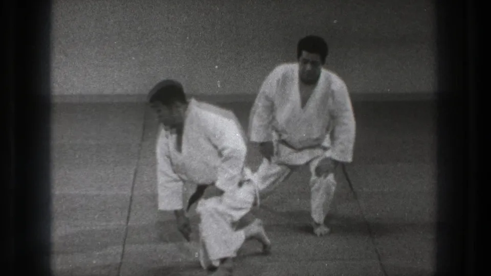 Near the end of the clip, two adult martial artists in white uniforms begin to stand after completing the grounded drill.